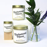 Large and mini Teakwood Moss scented soy candles pictured with bud vase and greenery.