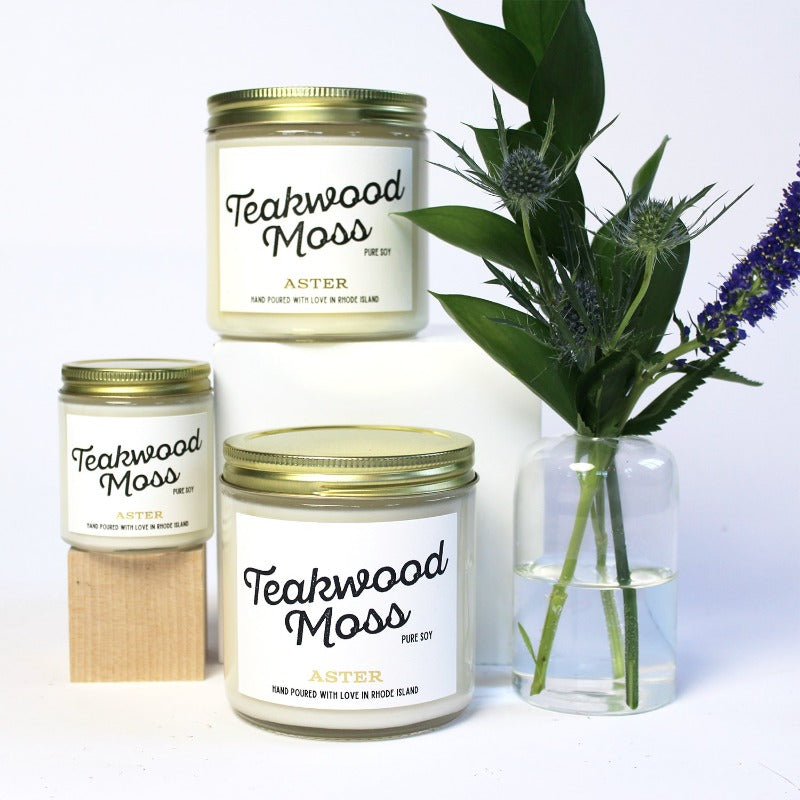 Large and mini Teakwood Moss scented soy candles pictured with bud vase and greenery.