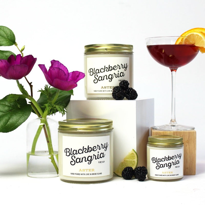 Large and mini Blackberry sangria scented soy candles pictured with flowers, fruit, and wine glass.