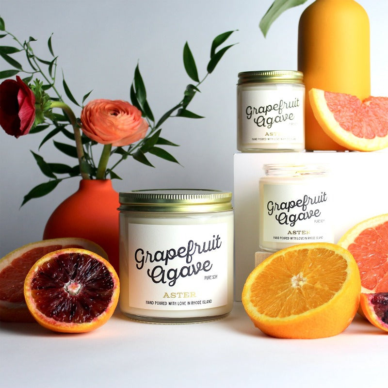 Large and mini Grapefruit Agave scented soy candles pictured with orange citrus fruits and flowers. 