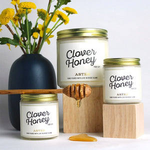 Large and mini Clover Honey scented soy candles pictured with flowers and honey spoon.