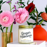 Mini Ginger Hibiscus scented soy candle pictured with vases of flowers and matches. 