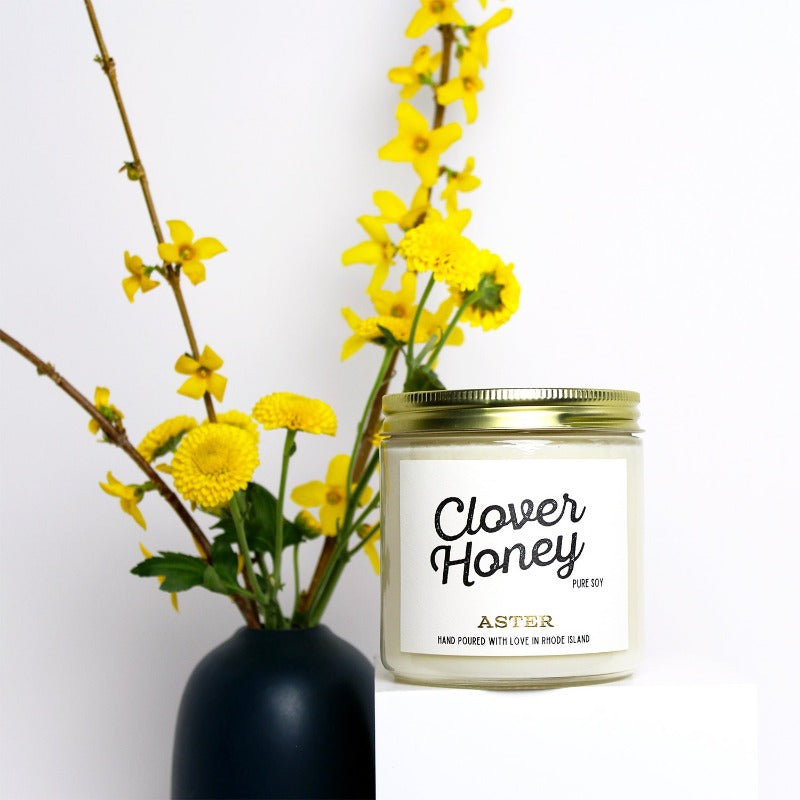 Large Clover Honey scented soy candle with vase of yellow flowers.