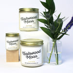 Large and mini Teakwood Moss scented soy candles pictured with bud vase and greenery. 